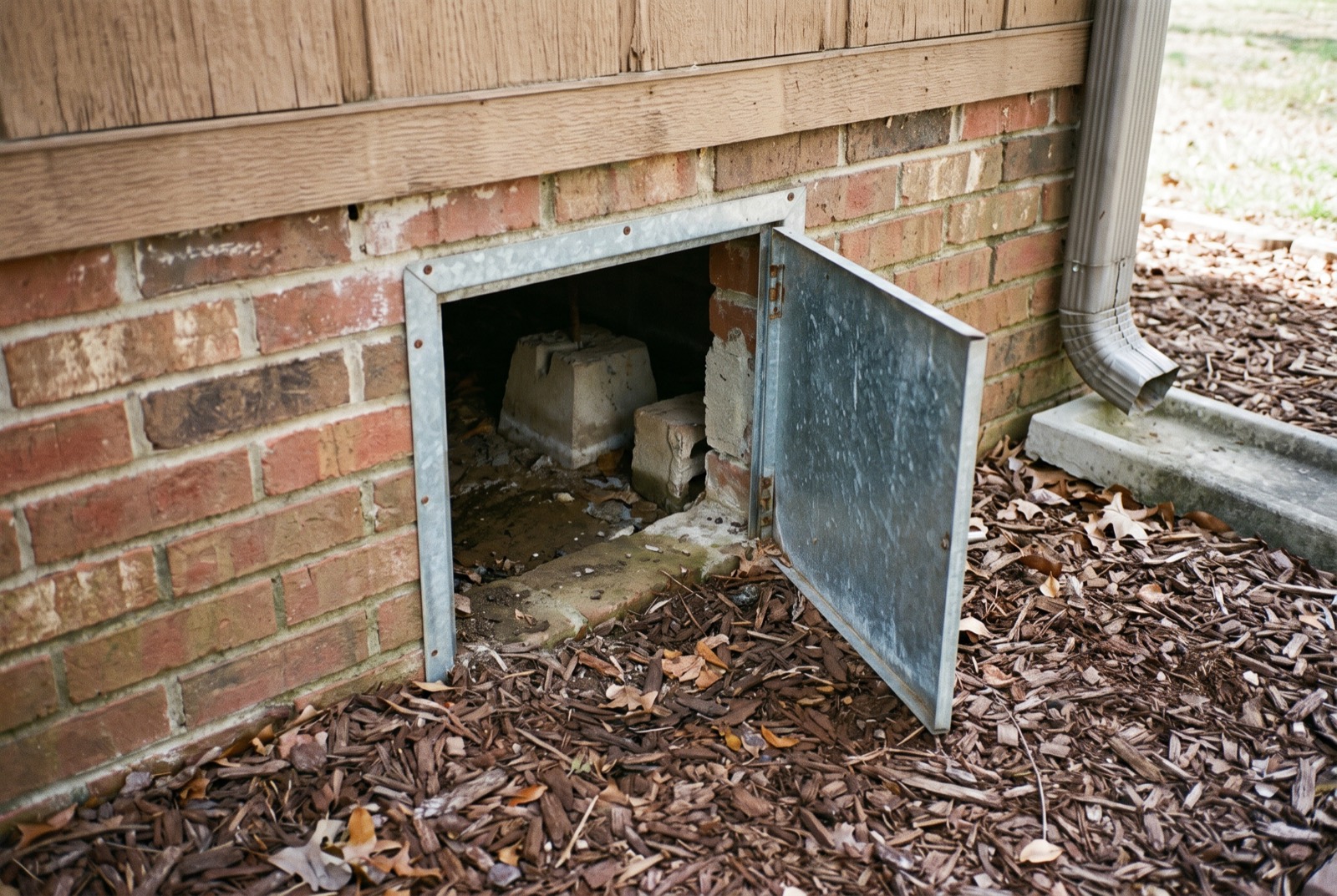 A brick-faced foundation wall with an open crawl space access door